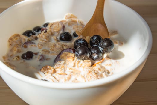 White bowl with healthy breakfast. Aronia and other berries with spelta  in milk