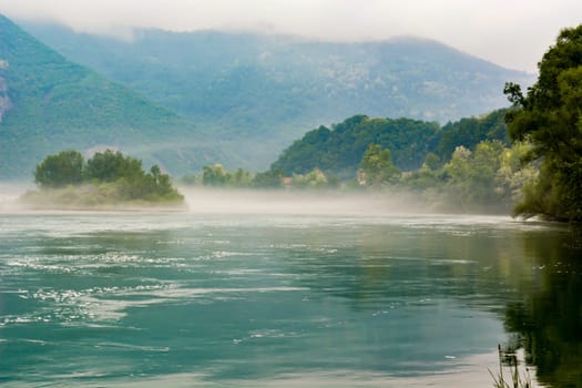 RIver Drina with haze in early morning. Cloudy mountain in background