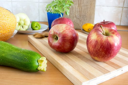 Group of apples on wooden plate, ready to be sliced and eaten. Various vegetables around the plate