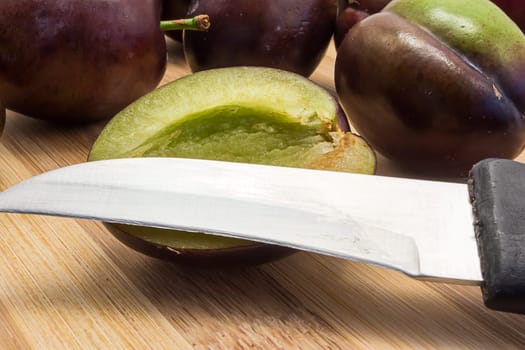 Juicy plum cuted in half on wooden board. Group of plums visible.