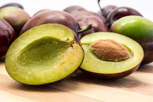 Juicy plum cuted in half on wooden board. Group of plums visible. Isolated on white background