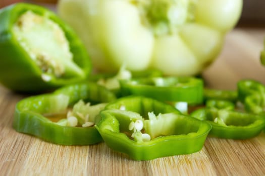 Sliced green pepper on wooden plate. Other vegetable is visible in the background
