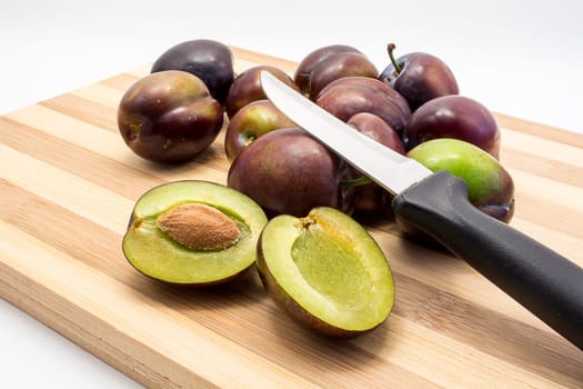 Juicy plum cuted in half on wooden board. Group of plums visible. Isolated on white background