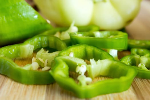 Sliced green pepper on wooden plate. Other vegetable is visible in the background