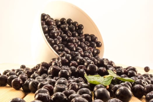 Fresh and tasty aronia spilled out of a bowl. Water droplets on fruit are visible