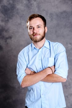 young bearded man with crossed arms in front of gray background