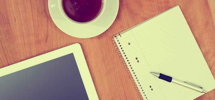 tablet PC, notepad with pen and a cup of tea on wooden table from above