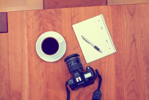 camera, notepad with pen and coffee on wooden table from above