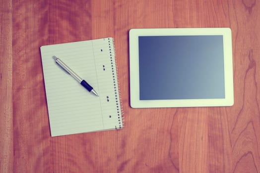 tablet PC and notepad with pen on wooden table from above