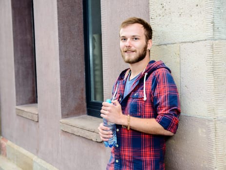 young bearded man with water bottle in checkered shirt in front of city- background