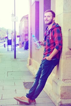 young bearded man with water bottle in checkered shirt in front of city- background