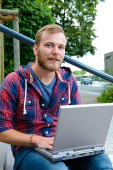 young man in checkered shirt sitting on stairs and using laptop