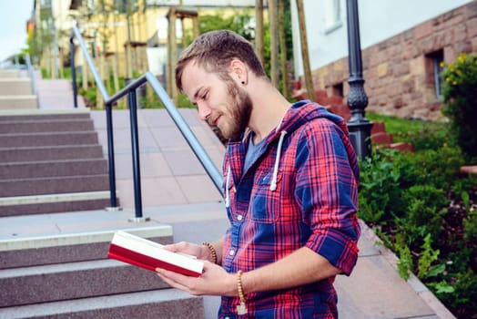 young man with beard standing with book and reading