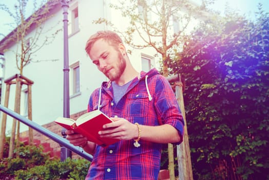 young man with beard standing with book and reading