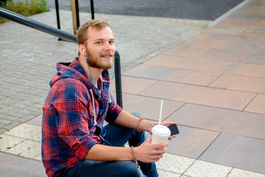 young man with soft drink sitting on stairs and using his smartphone