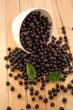 Fresh and tasty aronia spilled out of a bowl. Water droplets on fruit are visible