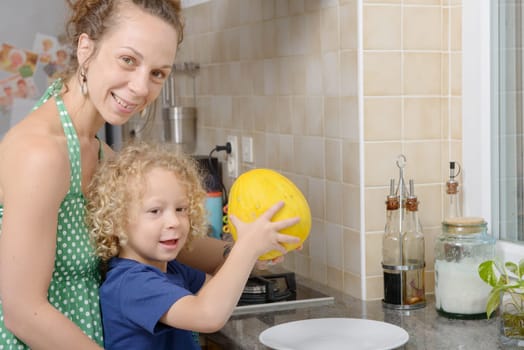 a child and his mother with a melon in kitchen