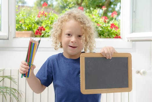 a blond and curly boy holding a chalkboard