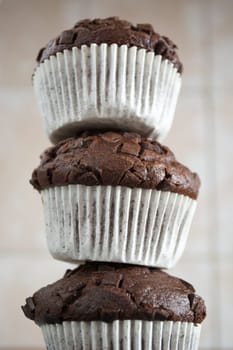 Three chocolate cupcakes stacked to form a tower in the kitchen