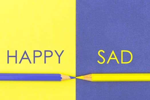 Happy versus Sad contrast concept. Yellow and Violet coloured pencils and paper.