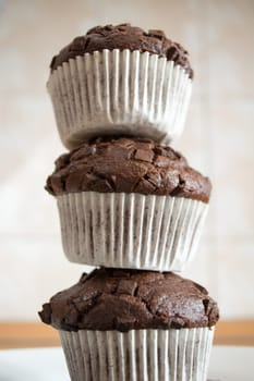 Three chocolate cupcakes stacked to form a tower in the kitchen