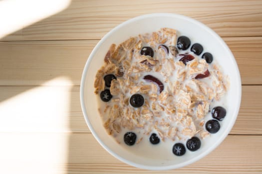 White bowl with healthy breakfast. Aronia and other berries with spelta  in milk