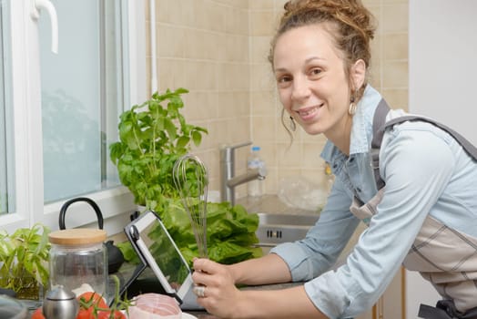 a smiling young woman using a tablet for cooking