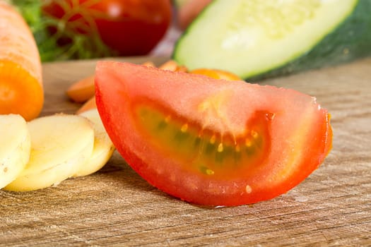 Sliced tomato on a wooden plate in the kitchen with various vegetables around