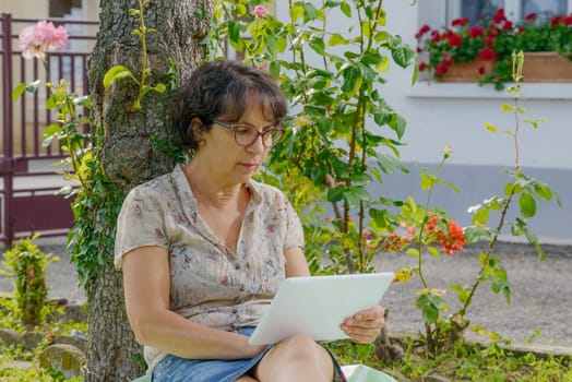 a mature woman sitting with a tablet in the garden