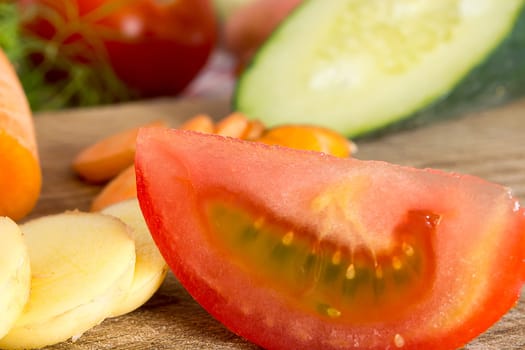 Sliced tomato on a wooden plate in the kitchen with various vegetables around