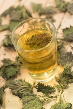 Glass of nettle tea. Table is covered with dry leaves. In tea is visible dry nettle leaf