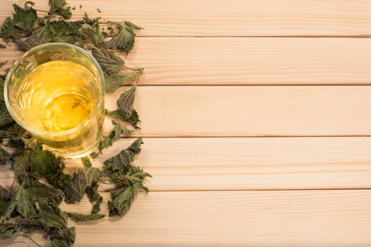 Glass of nettle tea. Table is covered with dry leaves.
