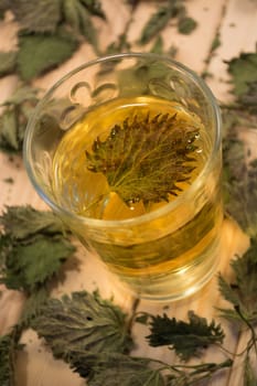 Glass of nettle tea. Table is covered with dry leaves. In tea is visible dry nettle leaf