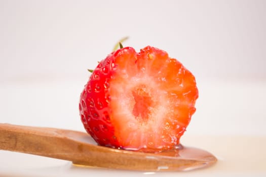 Bitten strawberry in wooden spoon with honey