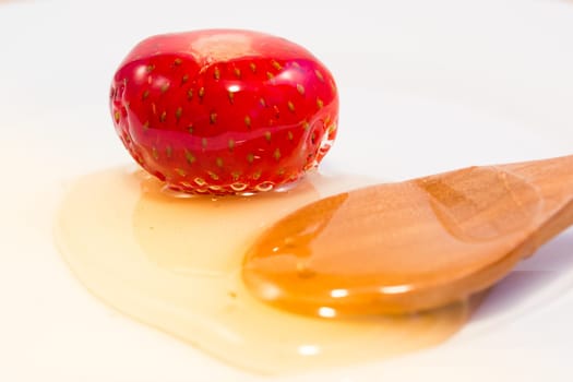 Strawberry covered with honey and spoon in ceramic white plate