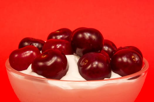 Vanilla cream with cherries on top in a glass cup on red background