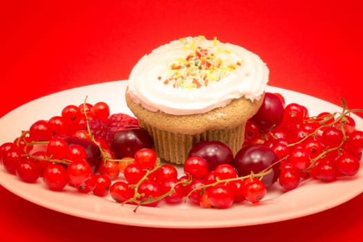 Cupcake with sweet crumbs surrounded by currant, cherries and raspberries on red background