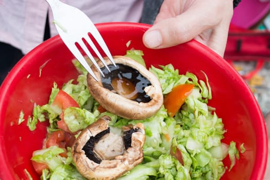 Ball filled up with fresh salad and grilled mushrooms. Barbecue visible in the background