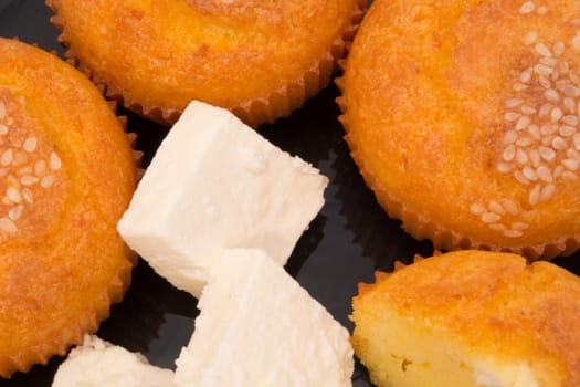 Black plate with muffins with sesame seeds on top isolated on white background. Chops of cheese also on the plate