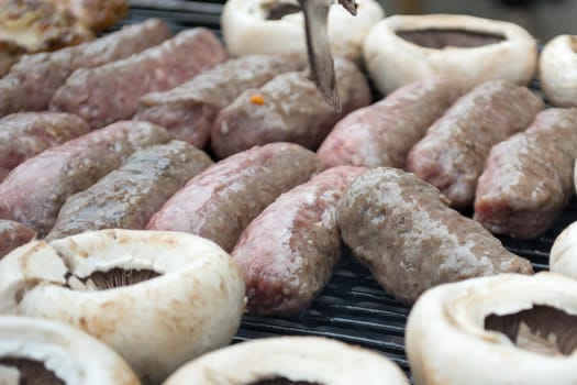 Grilling cevapi and mushrooms. Closeup. Smoke visible