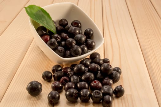 White bowl full with fresh and tasty aronia spilled on wooden table
