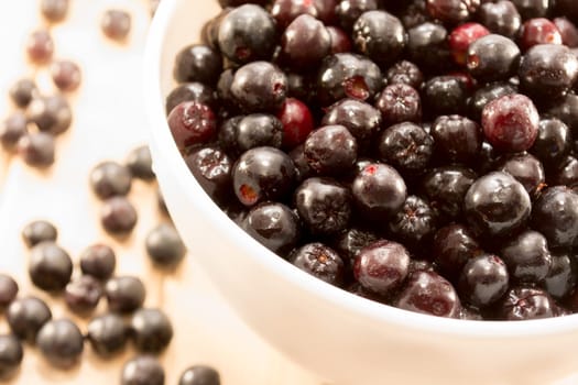 White bowl full with fresh and tasty aronia spilled on wooden table