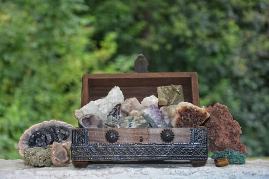 many minerals quartz and crystal stones in wooden box against green nature background