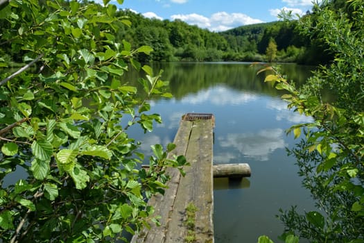Wooden jetted track on the lake with water reflection,blue sky with clouds