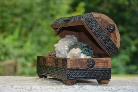many minerals quartz and crystal stones in wooden box against green nature background