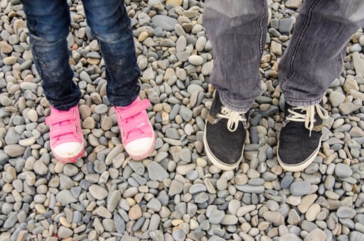Two pairs of feet in sneakers, adults and children, are on the pebble