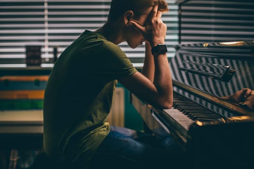 Teenager sitting at his piano with his head in his hands.