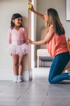 Little girl in a ballet costume having her height measure by her mother. She is standing against the wall whilst her mother uses the tape measure.