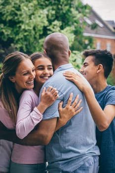 Happy family sharing a cuddle outdoors. Everyone is wrapping their arms round the father who has his back to the camera.