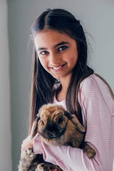 Portrait of a girl with her pet rabbit. She is holding it close to her and smiling at the camera.